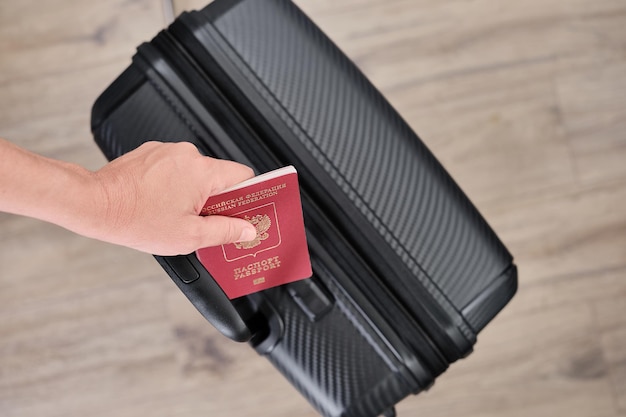 La mano de una mujer con un pasaporte ruso en el fondo de una maleta negra se alimenta desde arriba emigración de fondo borroso de la foto del país para un artículo o noticias