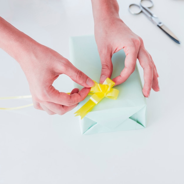 Mano de mujer pegando la cinta amarilla en una caja de regalo envuelta sobre un escritorio blanco