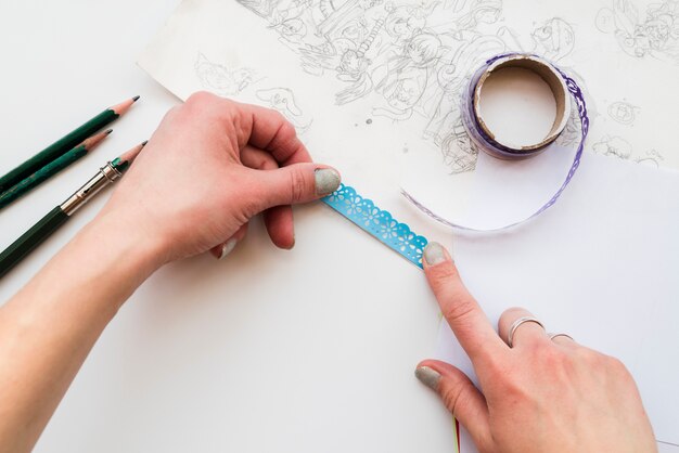 Mano de mujer pegando el encaje azul en papel de dibujo sobre el fondo blanco