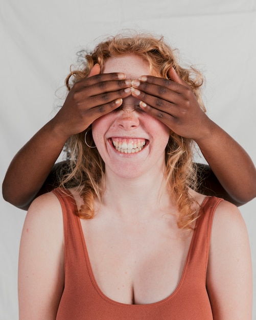 Foto gratuita mano de mujer de piel negra que cubre los ojos de su amiga justa contra un fondo gris