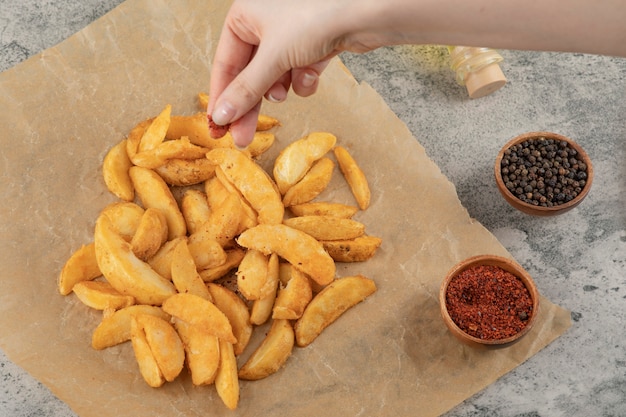 Foto gratuita mano de mujer poniendo pimienta en polvo a patatas fritas sobre papel vegetal.