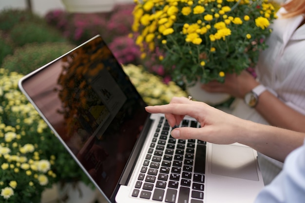 Mano de mujer presentando opciones de flores a un minorista de clientes potenciales usando laptop. Discusión de negocios, planificación de la colaboración futura mientras se anotan y negocian condiciones