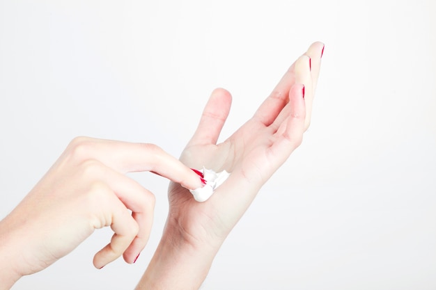 La mano de la mujer del primer con la crema hidratante aislada en el fondo blanco