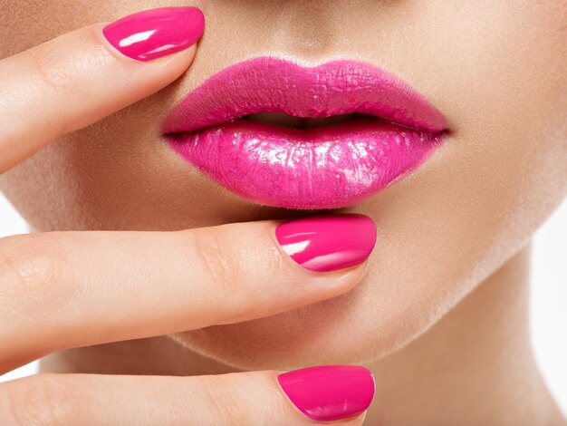Mano de mujer de primer plano con uñas rosadas cerca de los labios. Uñas con manicura rosa.