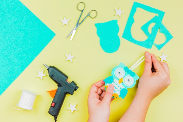 La mano de la mujer que hace el búho del papel de empapelar en fondo coloreado