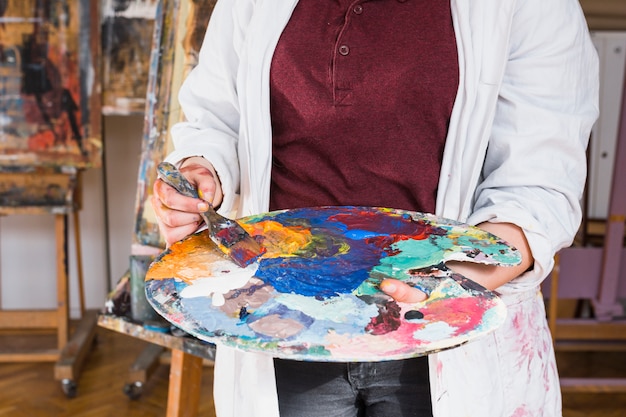 Mano de mujer que mezcla color de pintura de aceite en la paleta en el taller