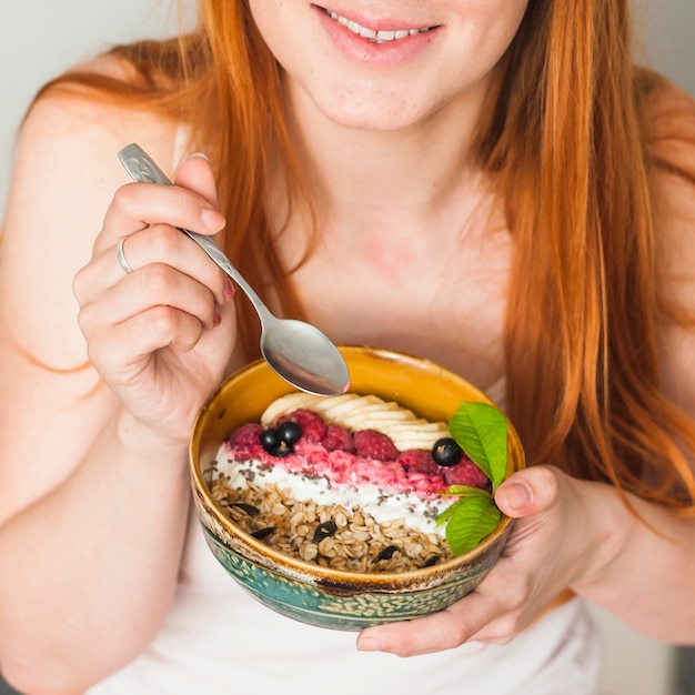 La mano de la mujer sonriente que sostiene el cuenco de granola de avena saludable con frutas