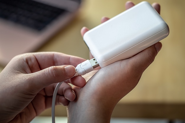 Mano de mujer sosteniendo cable usb blanco y banco de energía blanco