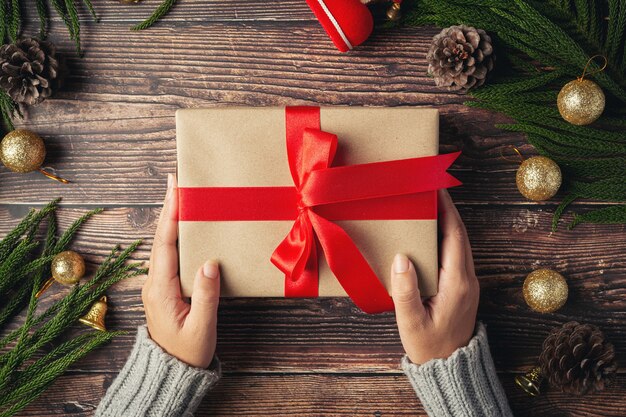 Mano de mujer sosteniendo una caja de regalo con cinta roja sobre un piso de madera