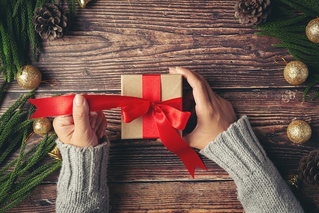 Mano de mujer sosteniendo una caja de regalo con cinta roja sobre un piso de madera