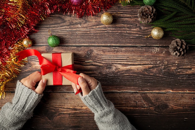 Mano de mujer sosteniendo una caja de regalo con cinta roja sobre un piso de madera