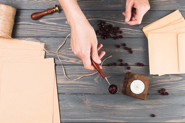 Foto gratuita mano de mujer sosteniendo un carrete de cera con material de artesanía sobre un escritorio de madera