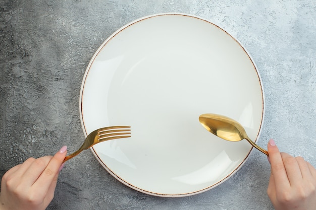 Mano de mujer sosteniendo cubiertos en plato vacío sobre superficie gris