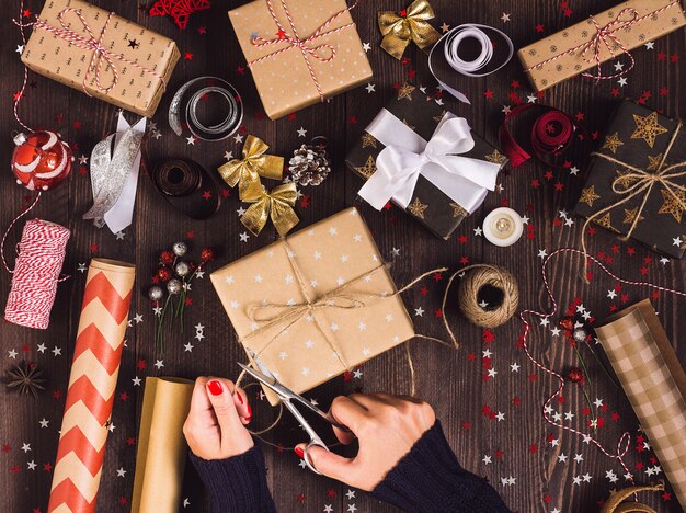 Mano de mujer sosteniendo una cuerda con tijeras para cortar y empaquetar caja de regalo de navidad