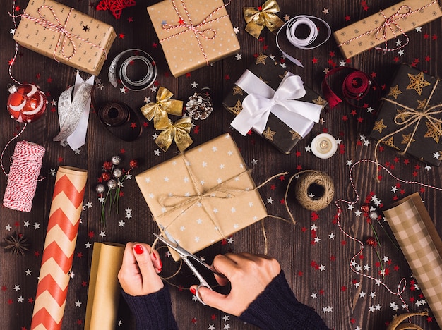 Mano de mujer sosteniendo una cuerda con tijeras para cortar y empaquetar caja de regalo de navidad