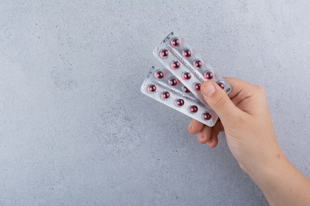 Mano de mujer sosteniendo dos paquetes de píldoras sobre fondo de mármol.