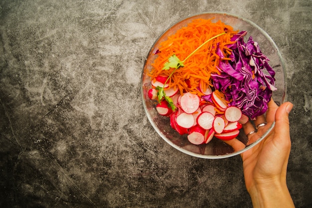 Mano de mujer sosteniendo ensalada fresca en un tazón sobre fondo grunge