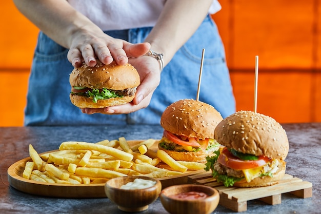 Una mano de mujer sosteniendo una hamburguesa con queso con patatas fritas, salsa de tomate, mayonesa