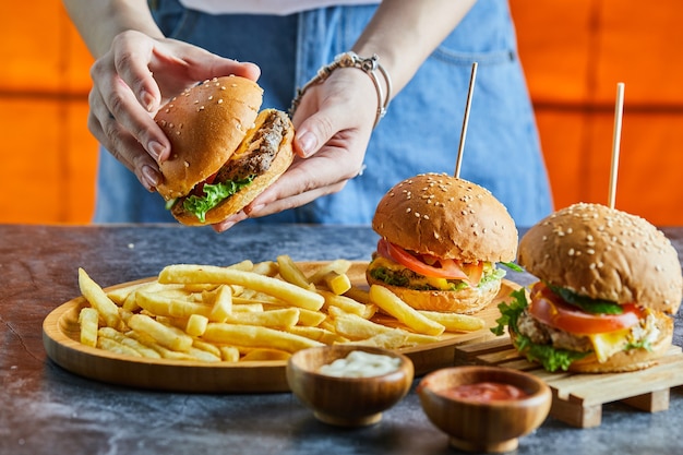 Una mano de mujer sosteniendo una hamburguesa con queso con patatas fritas, salsa de tomate, mayonesa