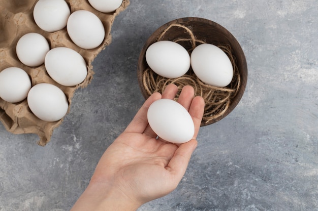 Mano de mujer sosteniendo un huevo de gallina blanco fresco sobre un fondo de mármol.