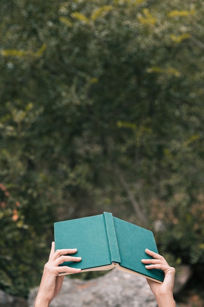 Mano de mujer sosteniendo un libro abierto en la mano contra árboles verdes