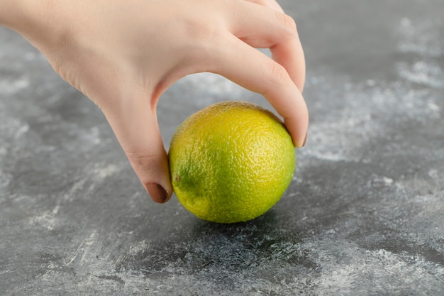 Mano de mujer sosteniendo un limón verde fresco.