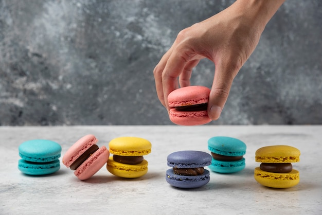 Foto gratuita mano de mujer sosteniendo macaron rosa sobre mesa blanca con docenas de macarons.