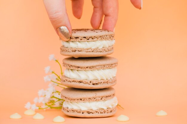 Mano de mujer sosteniendo macarrones con flor contra el fondo coloreado