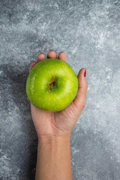 Mano de mujer sosteniendo manzana fresca en mármol.