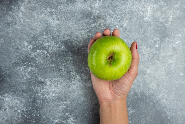 Mano de mujer sosteniendo manzana en mármol.