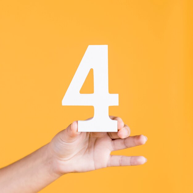 Mano de mujer sosteniendo el número 4 contra un fondo amarillo