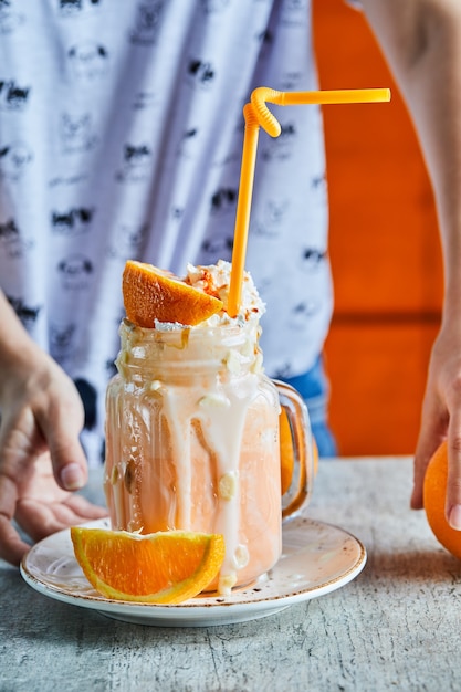 Una mano de mujer sosteniendo un plato blanco con batido de naranja y una rodaja de naranja