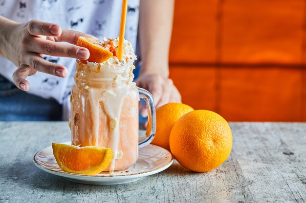 Una mano de mujer sosteniendo una rodaja de naranja y plato blanco con batido de naranja