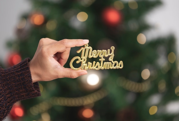 Mano de mujer sosteniendo texto de feliz Navidad para decorar un árbol de Navidad en el día de Navidad.