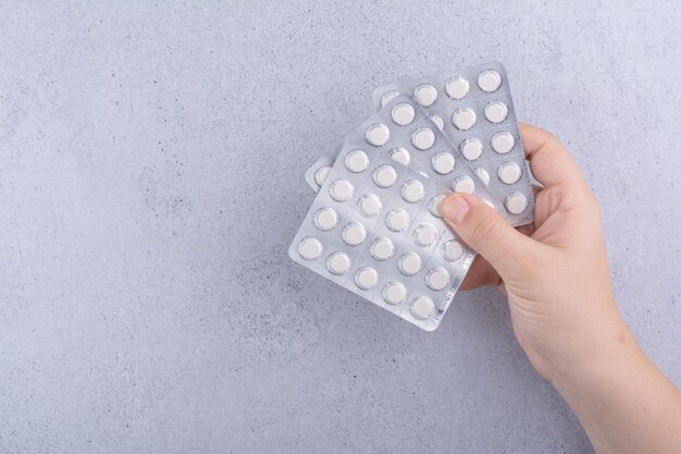 Mano de mujer sosteniendo tres paquetes de píldoras sobre fondo de mármol. Foto de alta calidad