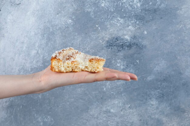 Mano de mujer sosteniendo un trozo de delicioso pastel sobre una mesa de piedra.