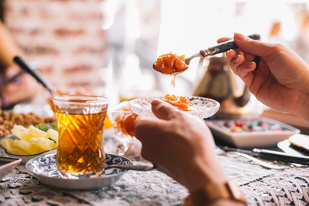 Mano de mujer sostiene una cuchara y una cacerola con mermelada de membrillo servido con té