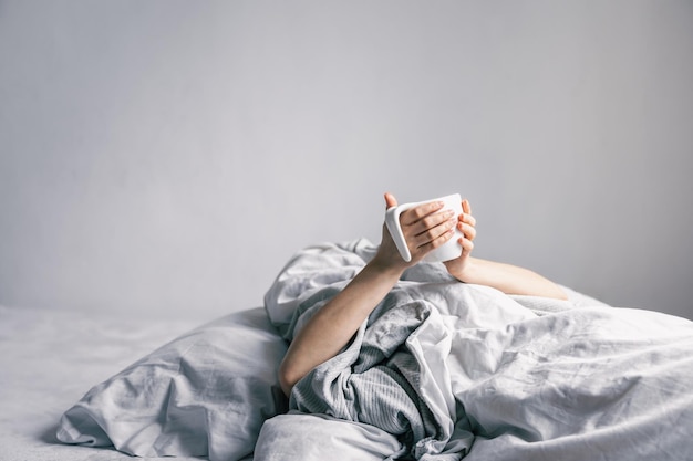 La mano de una mujer sostiene una taza de café mientras está acostada en la cama