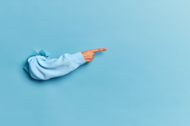 Mano de mujer en suéter azul rompiendo la pared de papel y apuntando al espacio de la copia