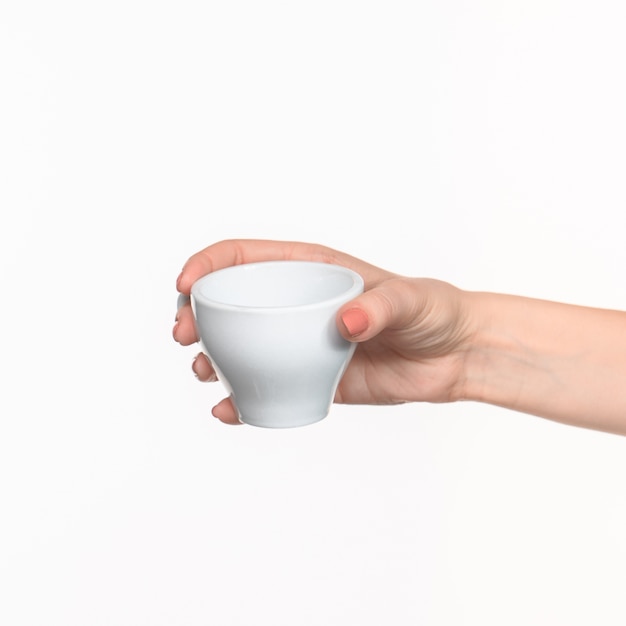 Mano de mujer con taza blanca perfecta sobre fondo blanco.