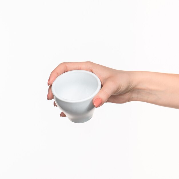 Mano de mujer con taza sobre fondo blanco.