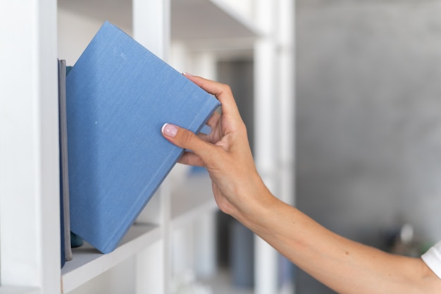 La mano de una mujer toma un libro de una estantería, elige qué leer en una noche de otoño de invierno