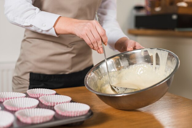 La mano de la mujer toma la mezcla para pastel con el cucharón del tazón de acero inoxidable