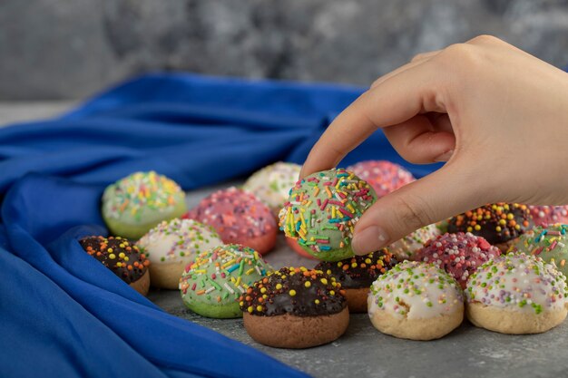 Mano de mujer tomando donut pequeño dulce colorido con chispitas.