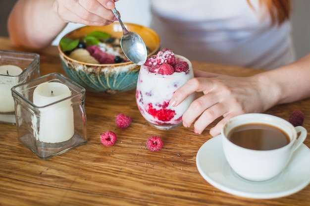 Mano de mujer con vaso de yogurt con frambuesas