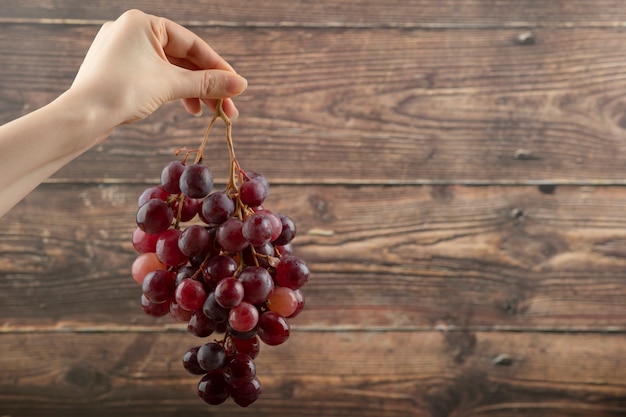 mano de niña sosteniendo racimo de uvas rojas en madera.