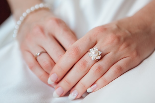Mano de novia con anillo de diamantes y pulsera de perlas en vestido blanco