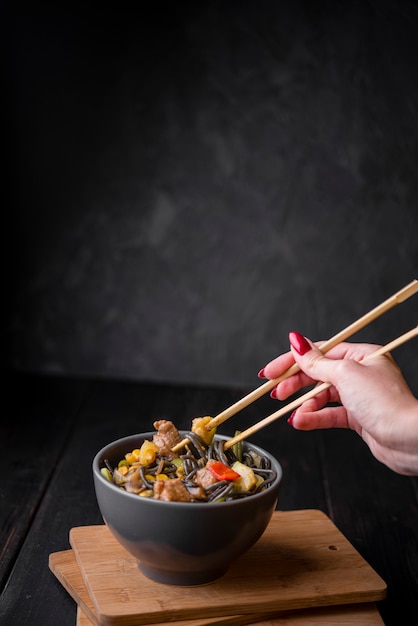 Mano con palillos mezclando en un tazón de fideos