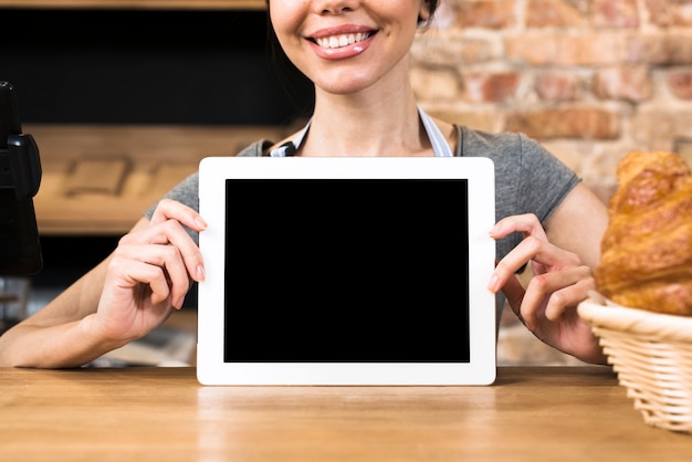 Mano del panadero femenino mostrando tableta digital de pantalla en blanco en la mesa