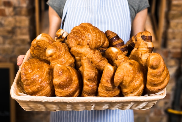 Foto gratuita mano del panadero femenino que sostiene la cesta de croissant al horno